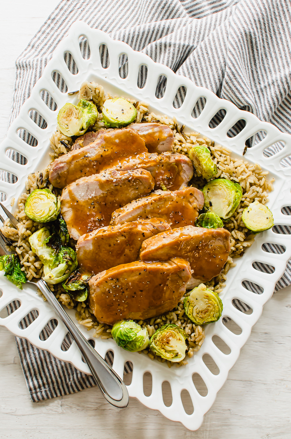 Maple glazed pork on a plate with Brussels sprouts and rice.