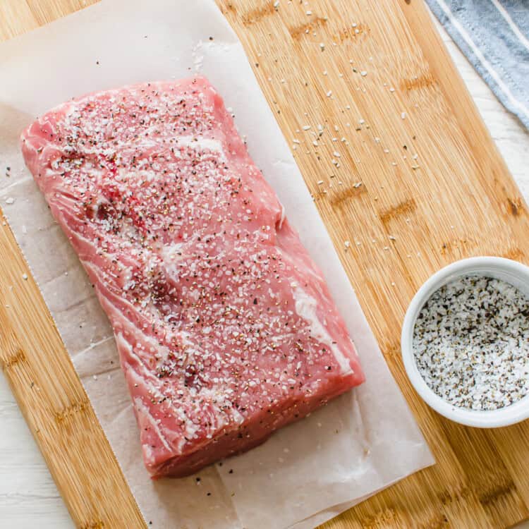 Pork loin on a wooden cutting board with salt and pepper on it.