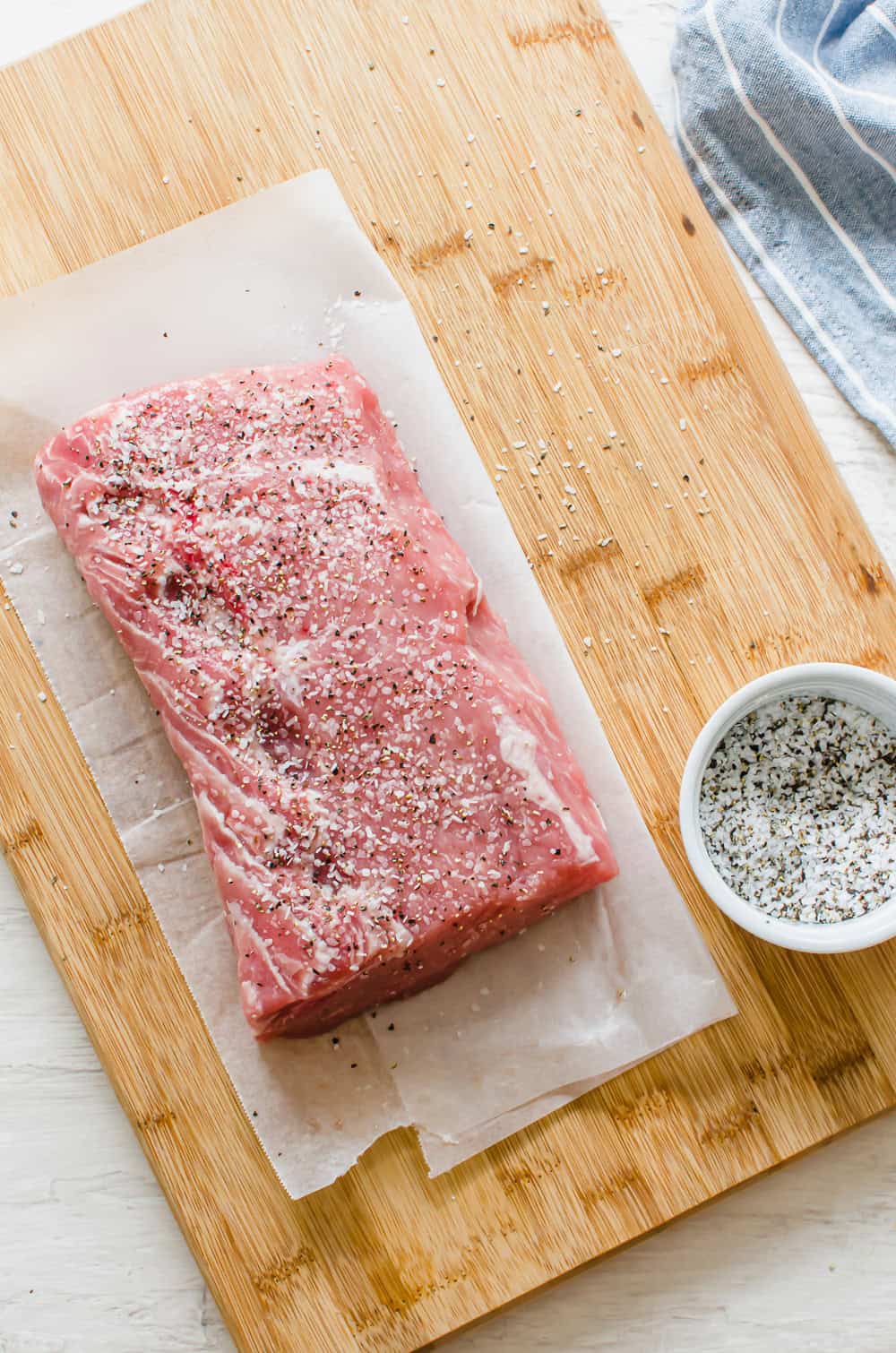 Pork loin on a wooden cutting board with salt and pepper on it.