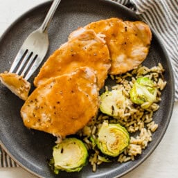 Maple glazed pork sliced on a plate with Brussels sprouts and rice.