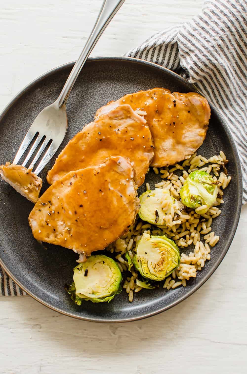 Instant Pot pork loin cooked and sliced on a plate with maple glaze with rice and Brussels sprouts on the side.