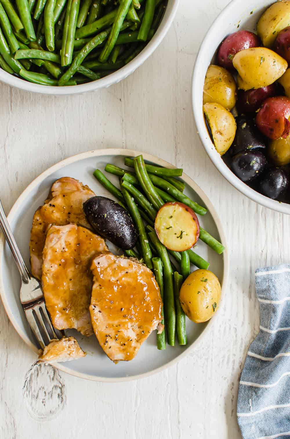 Sliced pork loin on a plate with green beans and potatoes.