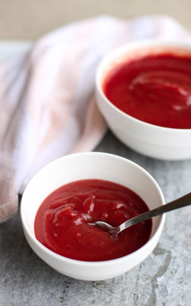 A spoon scooping apple cranberry sauce out of a white bowl 