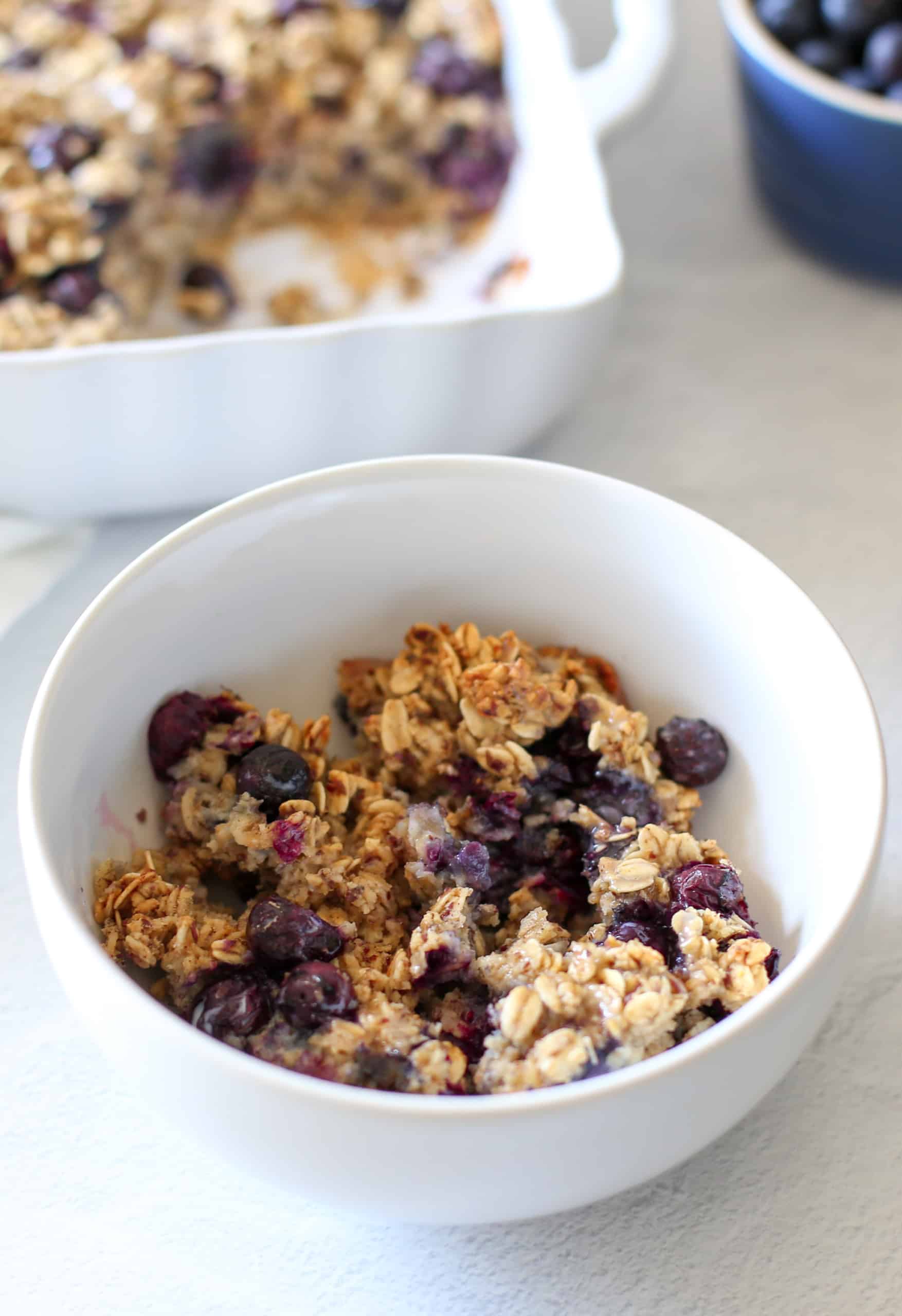 Blueberry baked oatmeal in a white bowl with milk over the top of it. 
