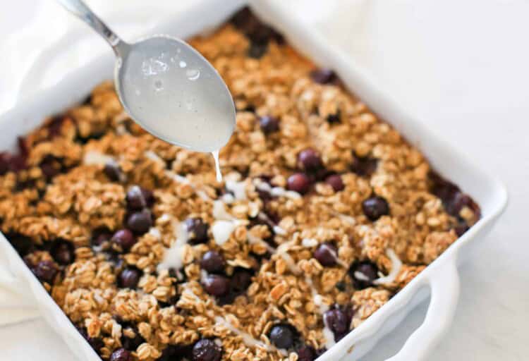 spoon drizzling icing on blueberry baked oatmeal