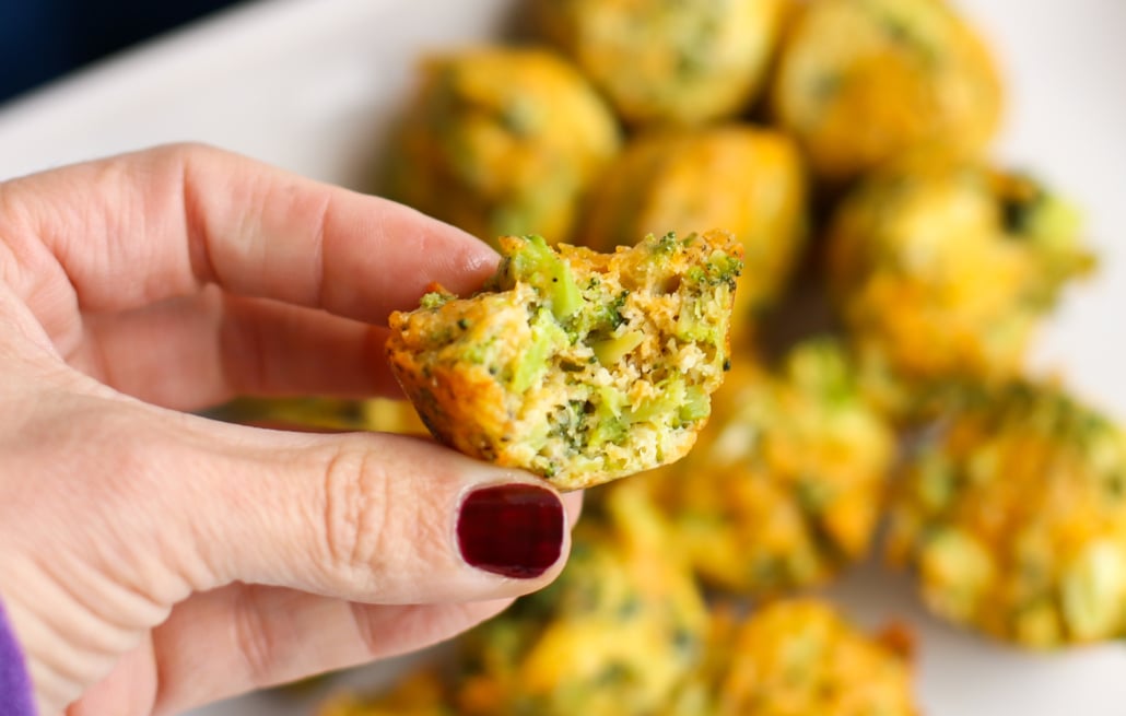 woman's hand holding a broccoli cheddar bite that has a bite taken out of it