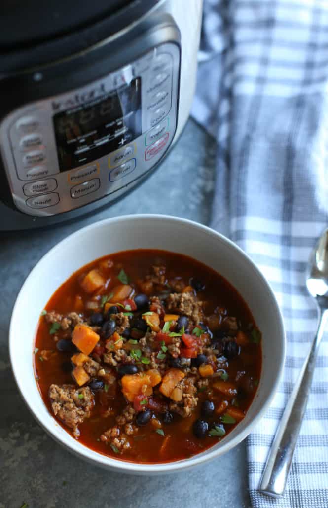 Turkey Chili with sweet potato and black beans in a white bowl with and Instant Pot in the background
