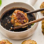 Chop sticks holding an Asian turkey meatball above a small bowl of sweet soy dipping sauce.