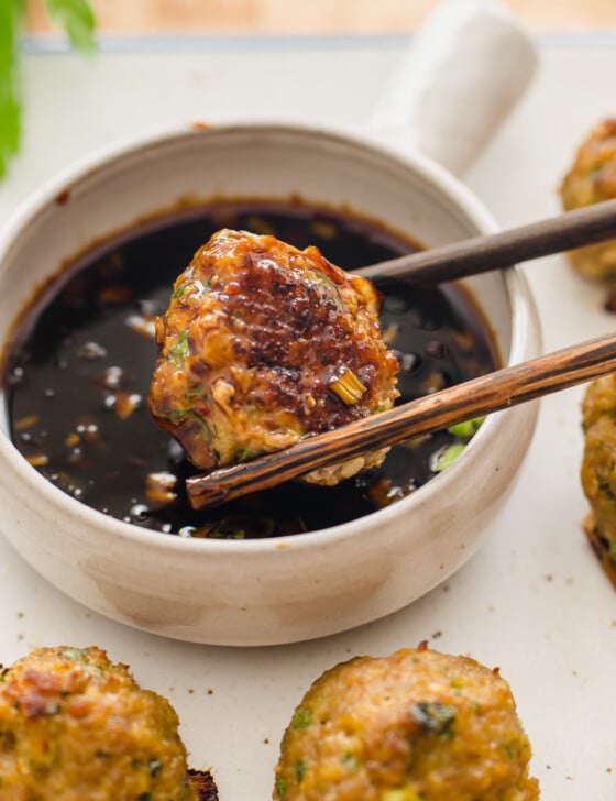 close up shot of chop sticks holding a turkey meatball and dipping in sauce