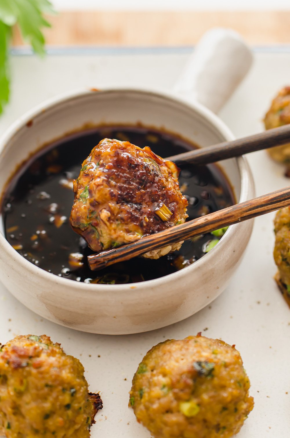 close up shot of chop sticks holding a turkey meatball and dipping in sauce