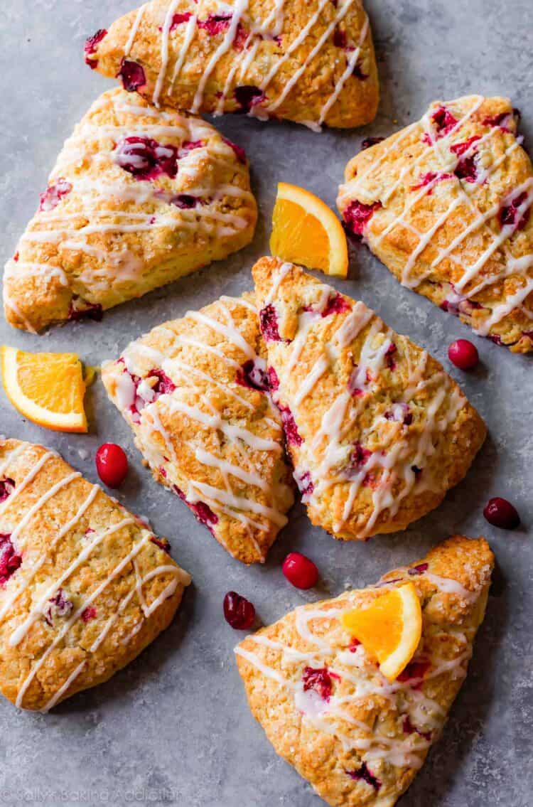 Cranberry orange scones on a gray counter with fresh cranberries and small orange segments.