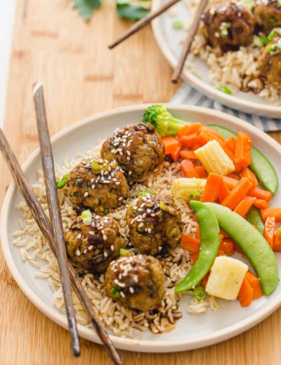 asian meatballs on a plate with stir fry veggies as a side and chop sticks laying on the plate