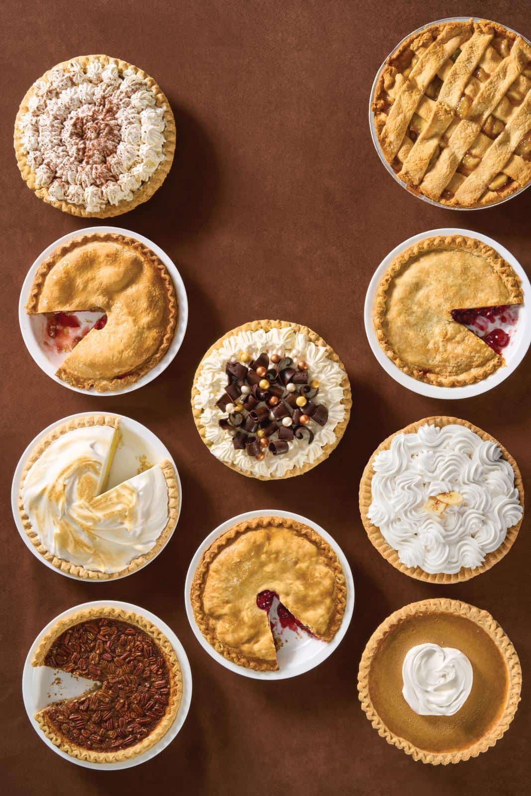 10 varieties of pies on a table some with a slice out of them.