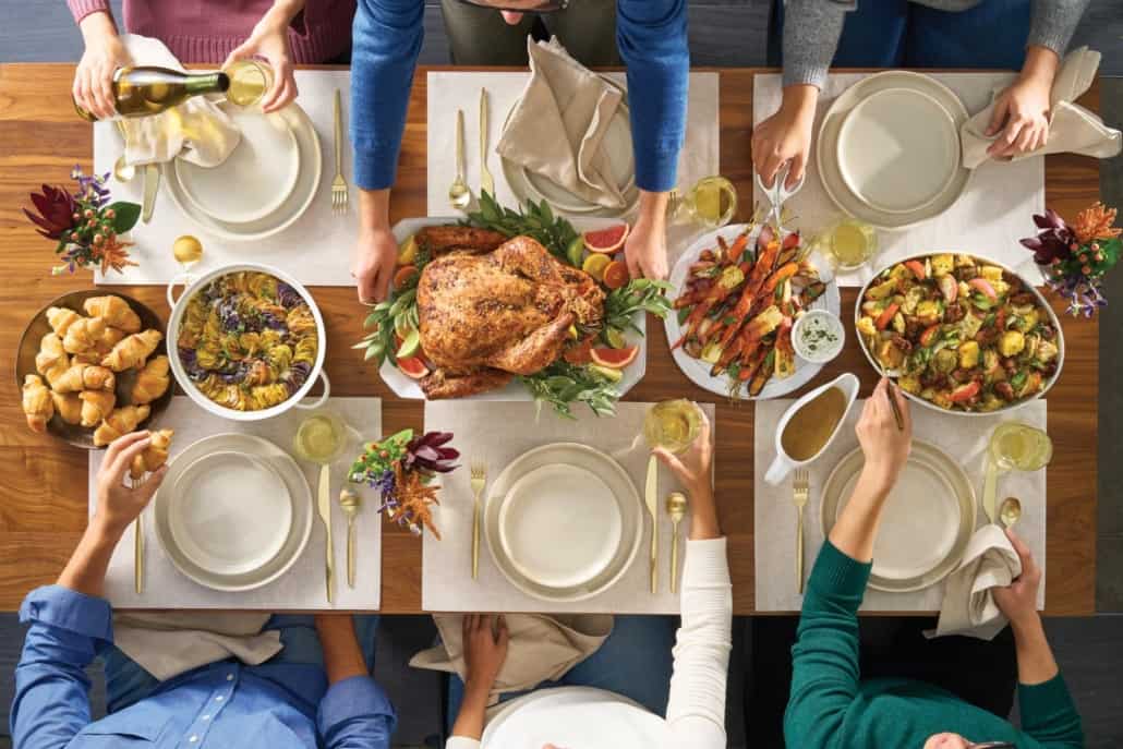 Thanksgiving table with people seated around it who are passing the dishes around.