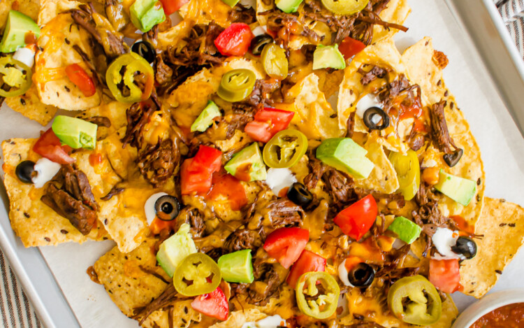 Shredded Beef Nachos on a pan with toppings ready to be served.