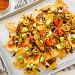 Shredded beef nachos on a sheet pan with toppings added ready to serve.