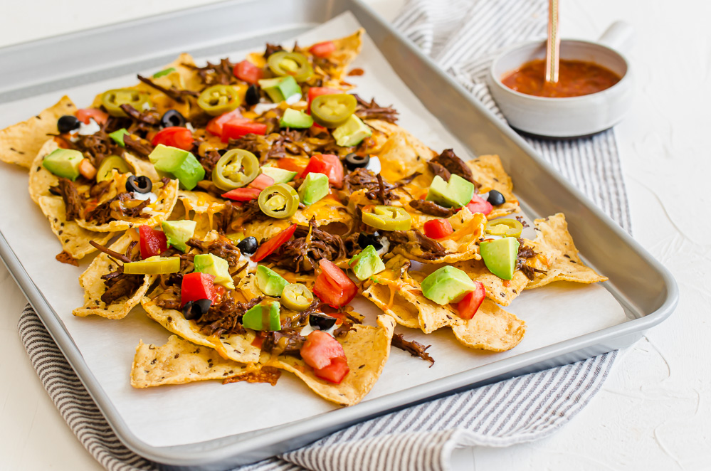 shredded beef nachos on a sheet pan with Mexican toppings