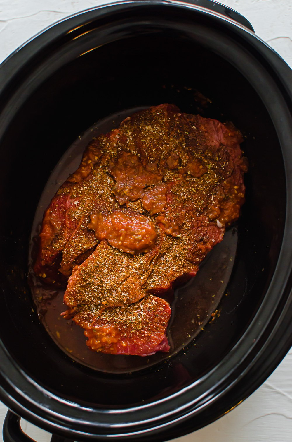 Seasoned chuck roast in a slow cooker with salsa poured over top.