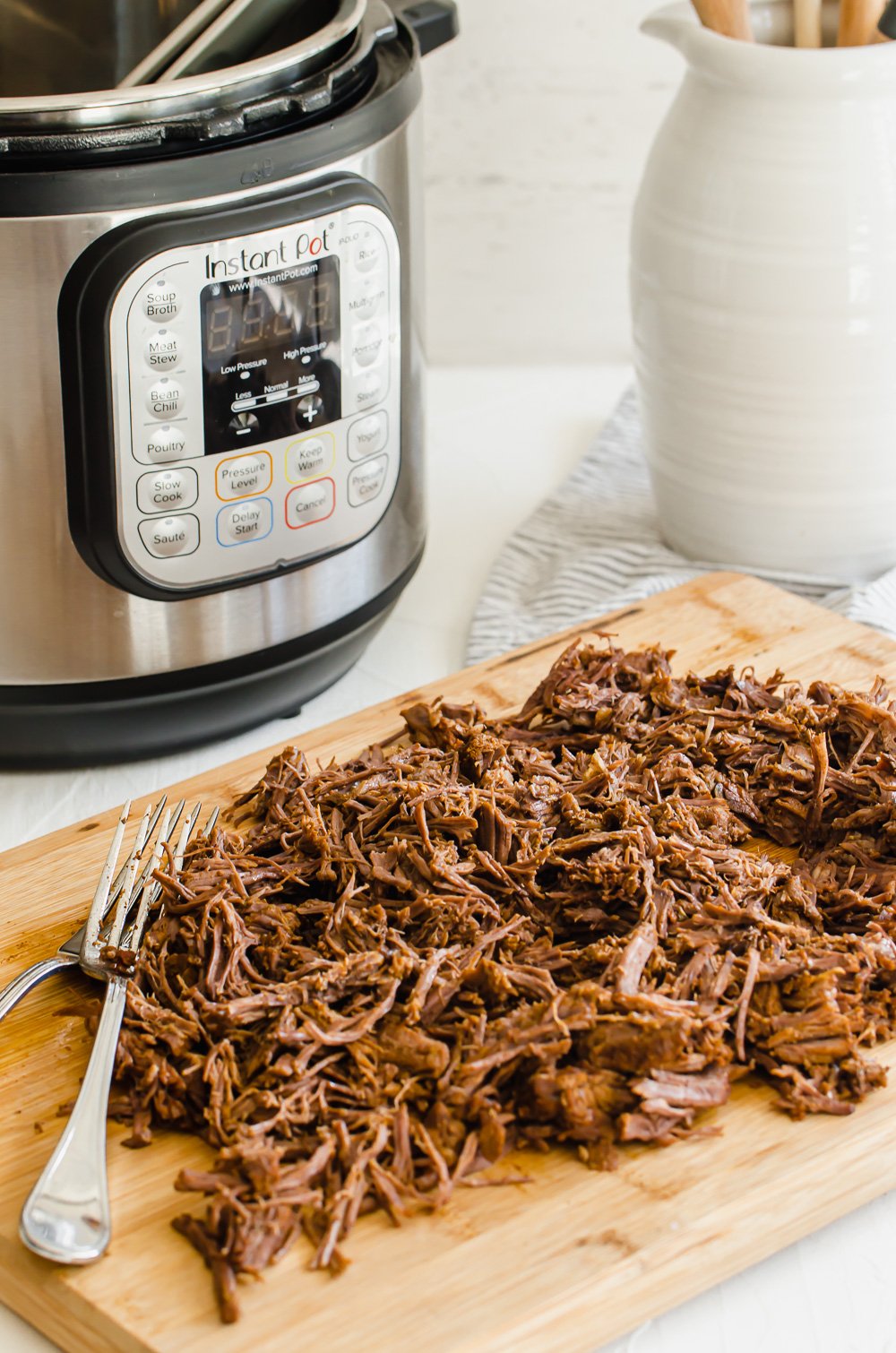 Shredded beef on a wooden cutting board with an Instant Pot in the background.