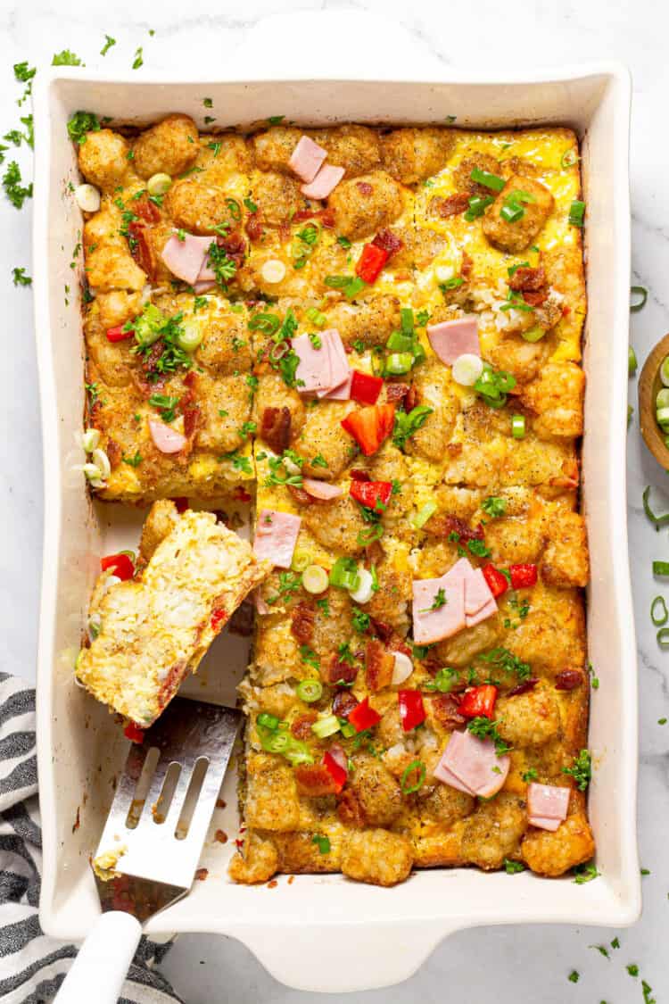 Tater Tot Breakfast Bake in a white casserole dish with a portion being lifted out with a small spatula.