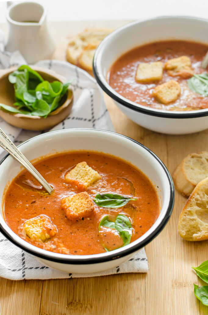 Vertical shot of tomato bisque in bowls with croutons and basil on top