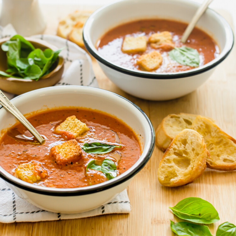 Two bowls of tomato soup with croutons and fresh basil on top.