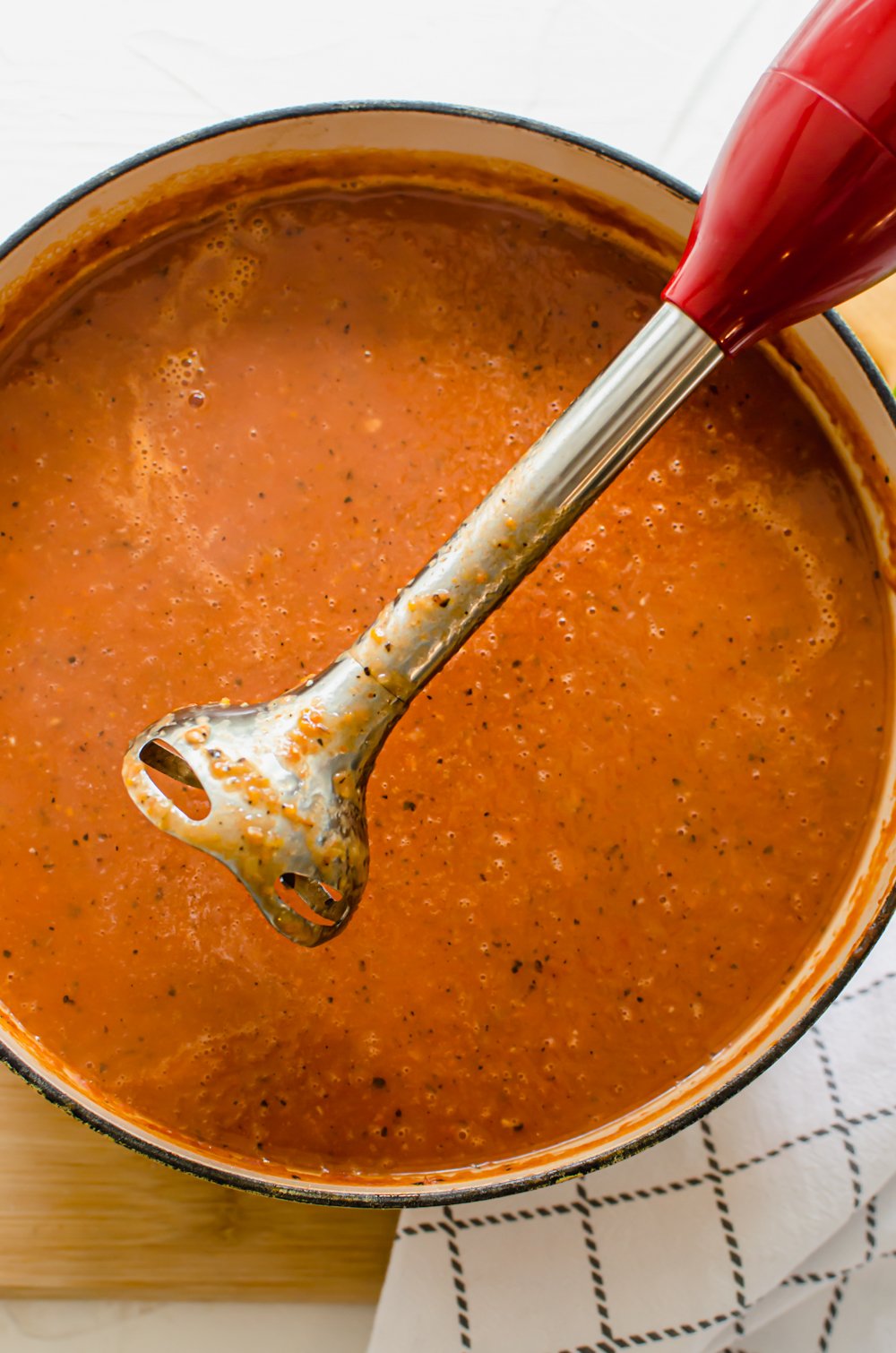 process shot of using an immersion blender in a pot of tomato bisque soup.