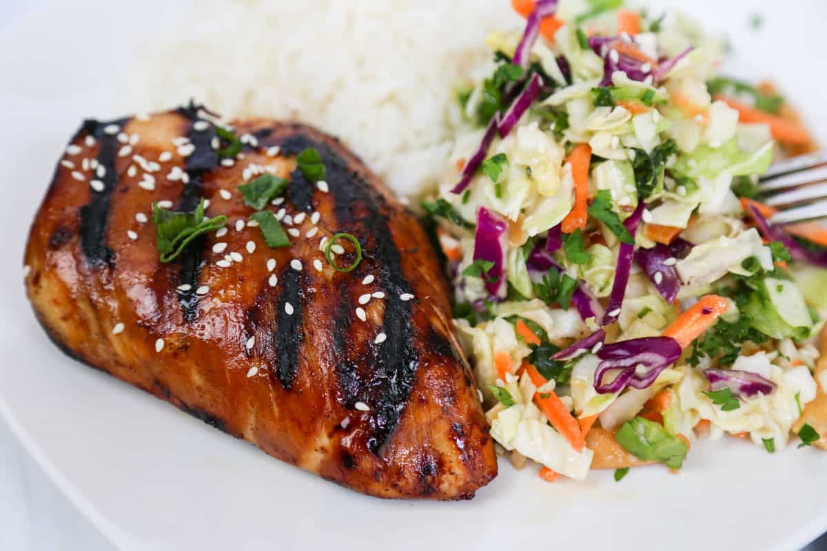 Whole grilled asian chicken on a plate with slaw and rice.