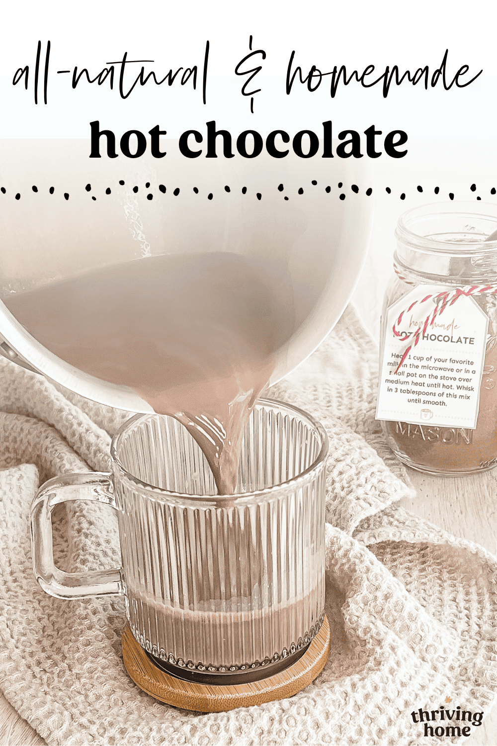 Homemade hot chocolate being poured from a pan into a glass mug with a jar of hot chocolate mix in the background.