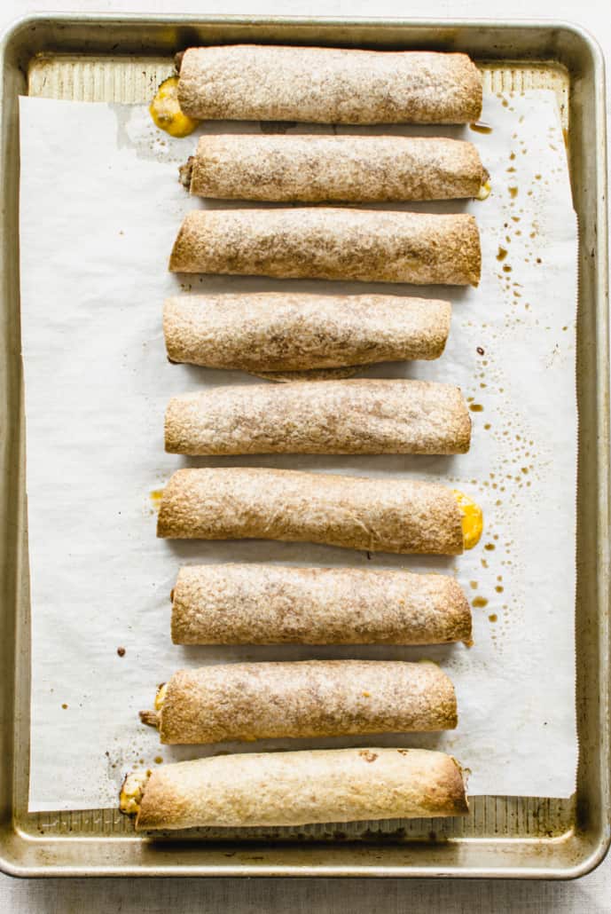 Baked and rolled beef taquitos on a baking sheet lined with parchment paper.