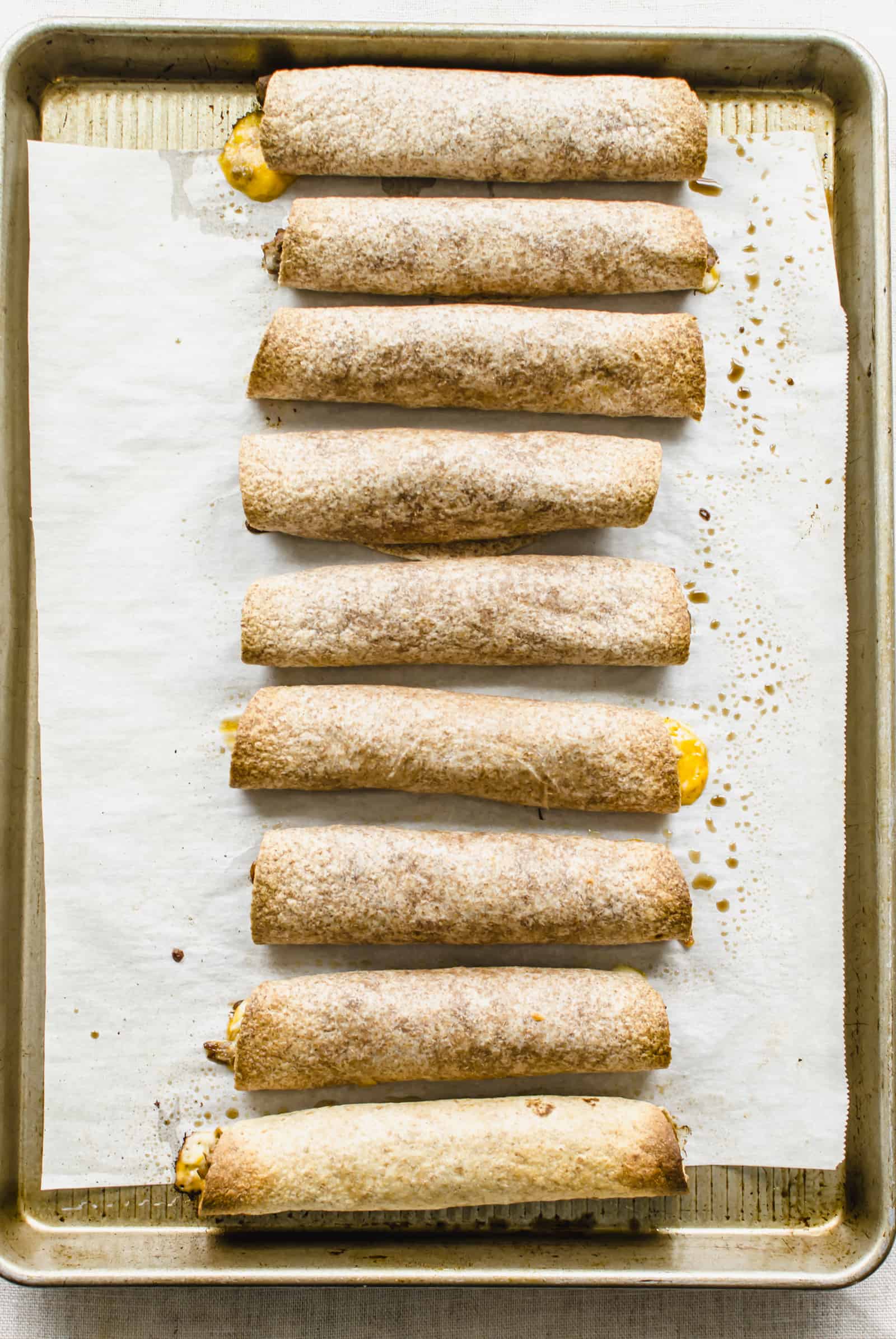 Cooked beef taquitos on a baking sheet lined with parchment paper.