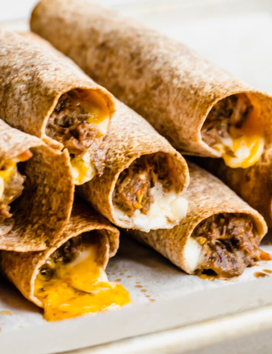 Stack of beef taquitos with cheese melting out of them.