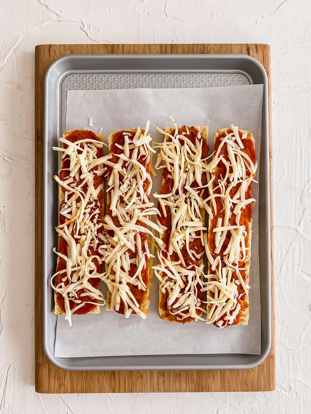 Sliced baguettes on a baking sheet with pizza sauce and shredded mozzarella.