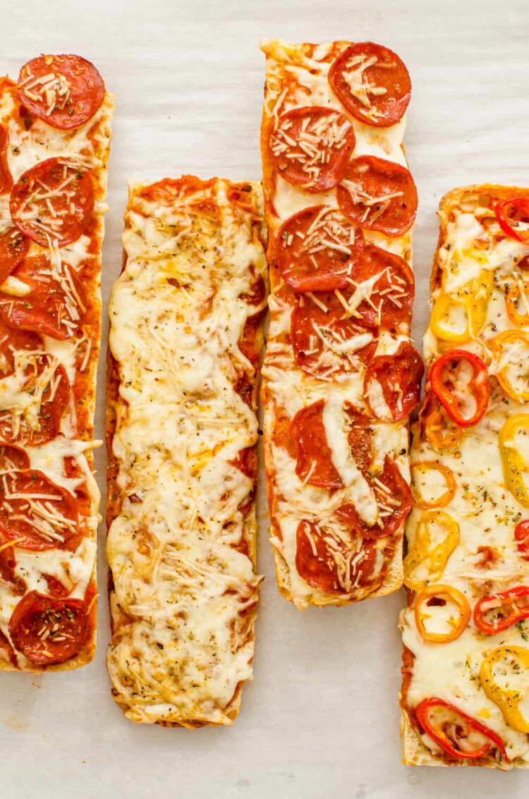 French bread pizzas lined up, two with pepperoni, one with cheese, and one with bell peppers.
