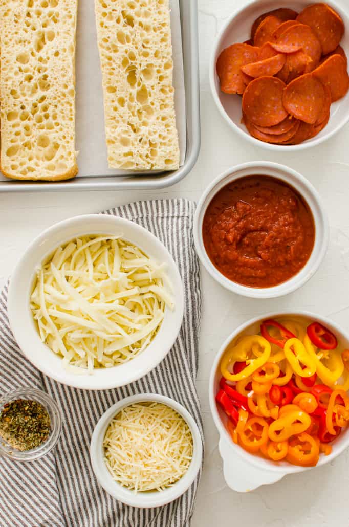 Toppings for pizza bread spread out in white bowls