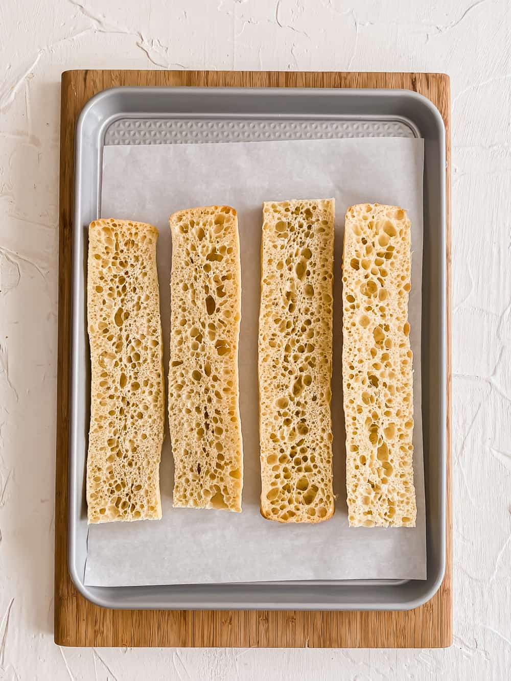 Sliced baguettes on a parchment-lined baking sheet.