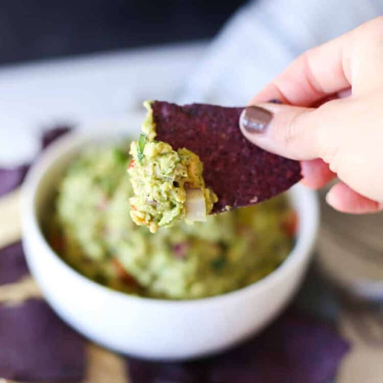 A hand dipping a chip into a bowl of guacamole.