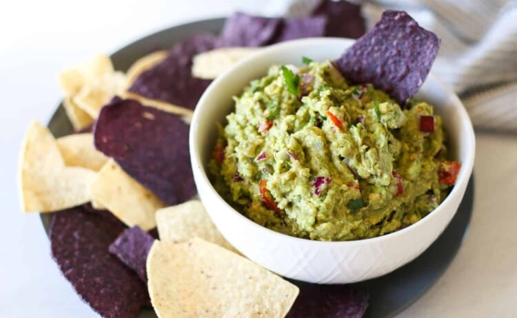 Homemade guacamole in a bowl with blue corn chips around it.