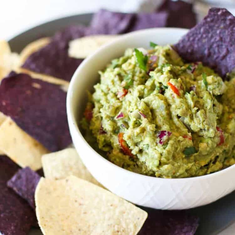 Homemade guacamole in a bowl with blue corn chips around it.