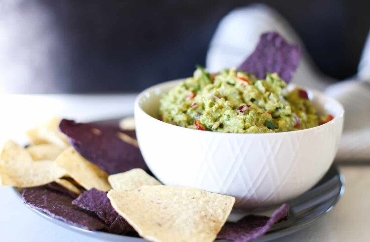 Bowl of guacamole with white and blue corn chips around it.