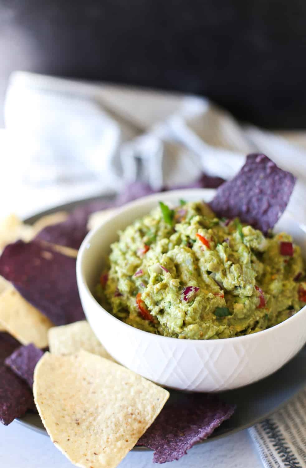 Guacamole in a white bowl with a blue corn chip being dipped into it.