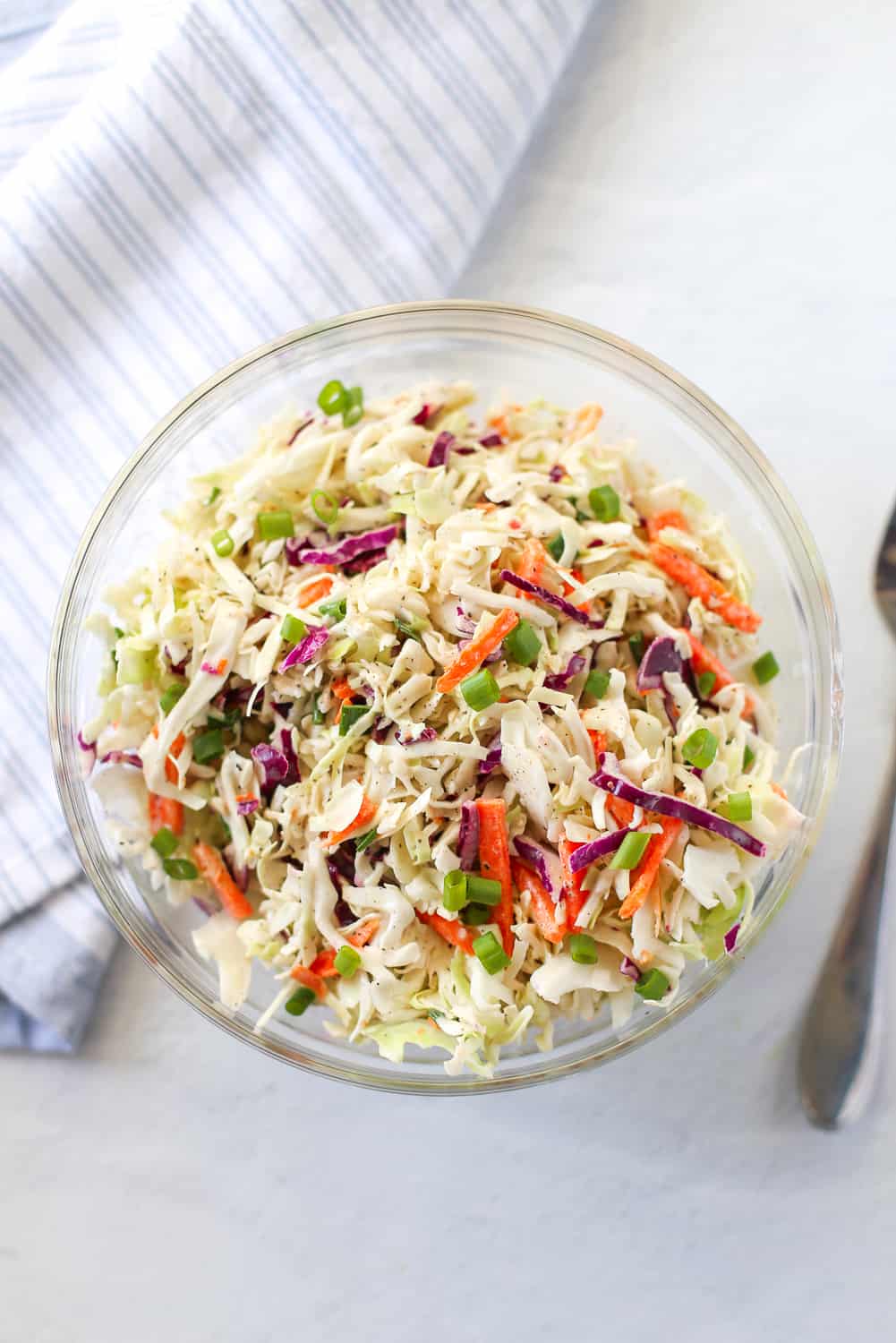 Coleslaw for pulled pork in a glass bowl with chopped green onions on top.