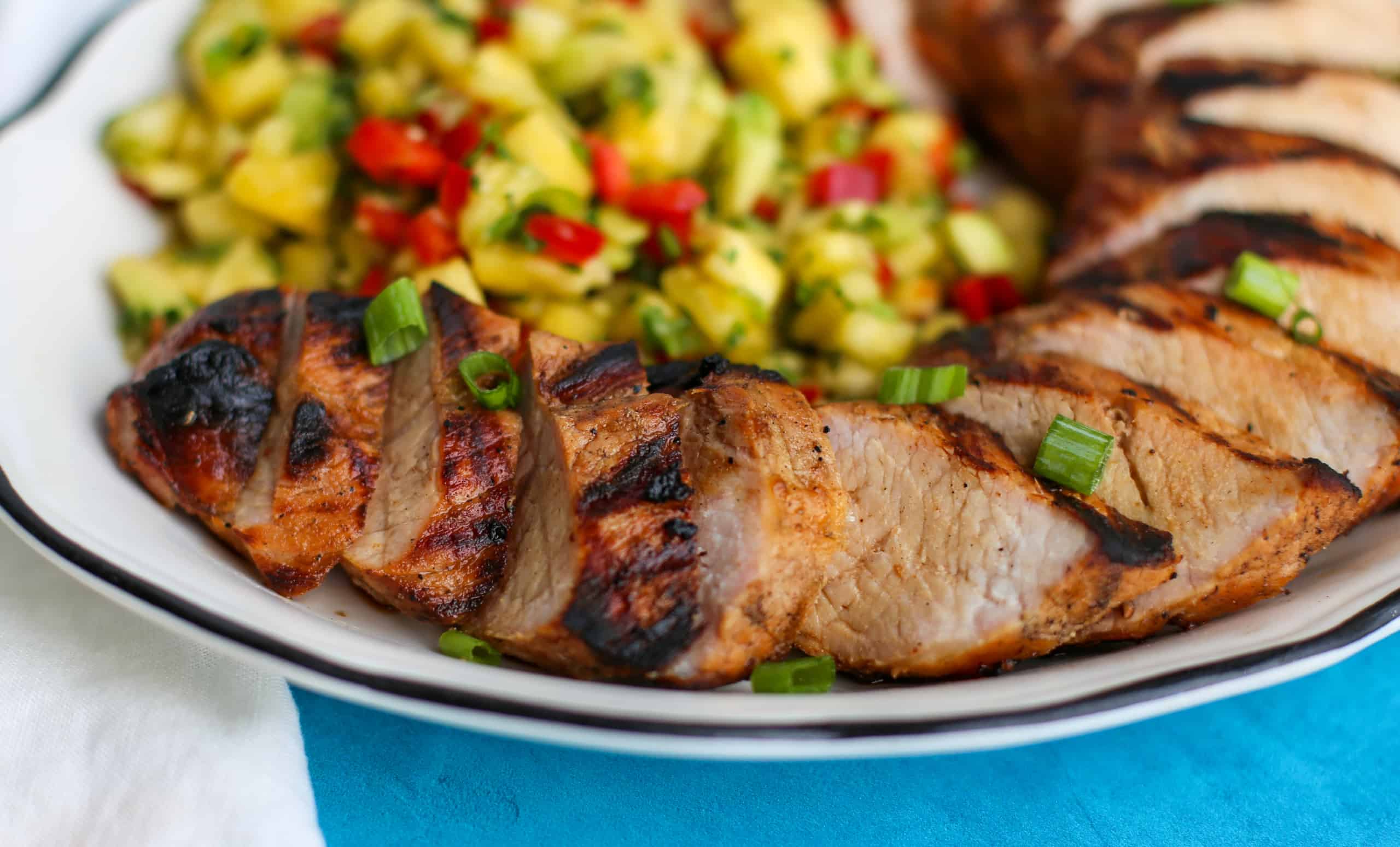 Sliced Hawaiian grilled pork tenderloin fanned out on a plate with Pineapple Salsa.