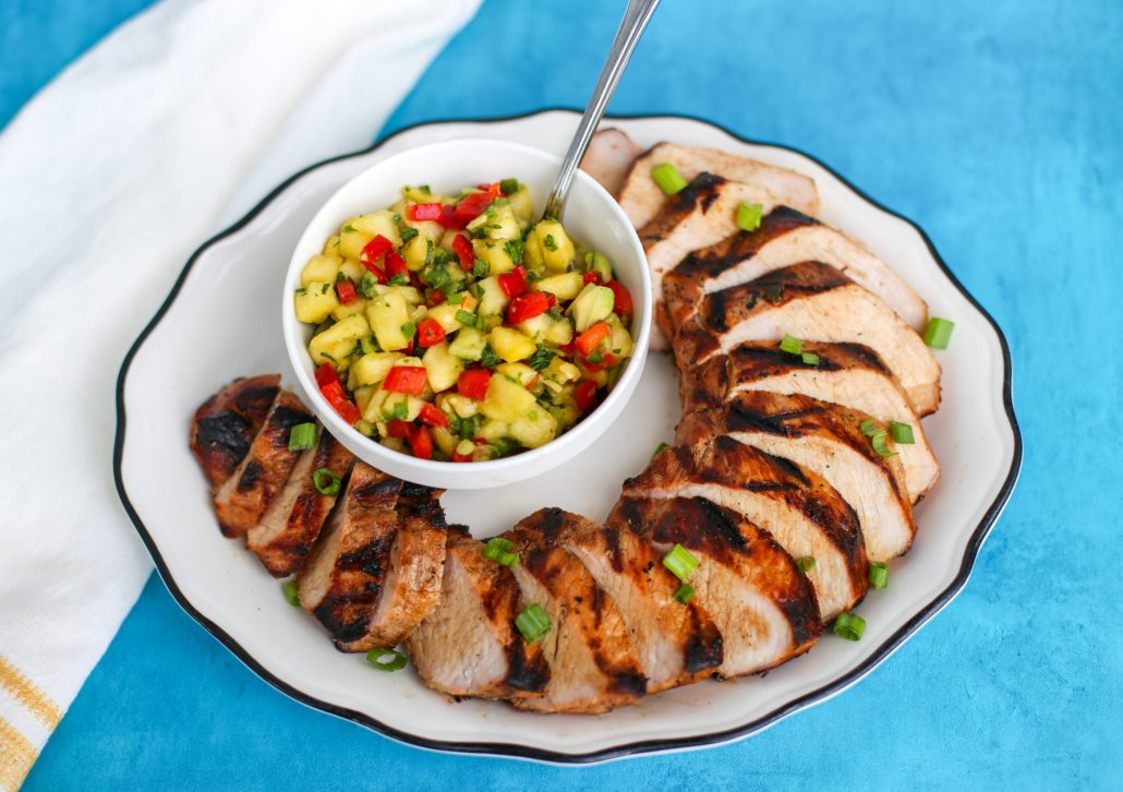 A cooked and sliced grilled pork tenderloin with a side of pineapple salsa.