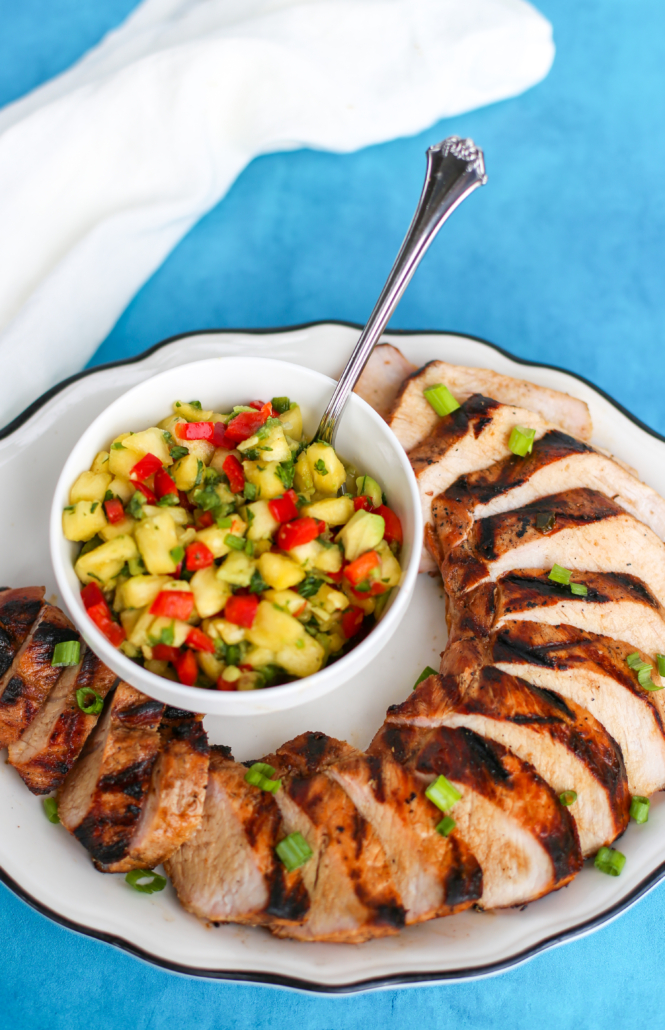 Pineapple salsa in a white bowl surrounded by grilled pork tenderloin