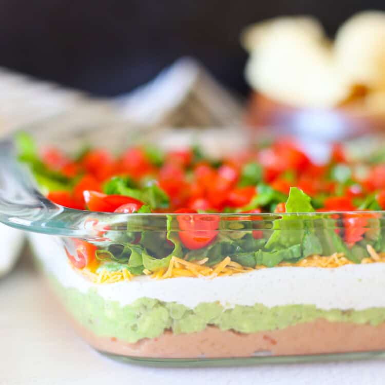 Layered taco dip in a square glass baking dish.