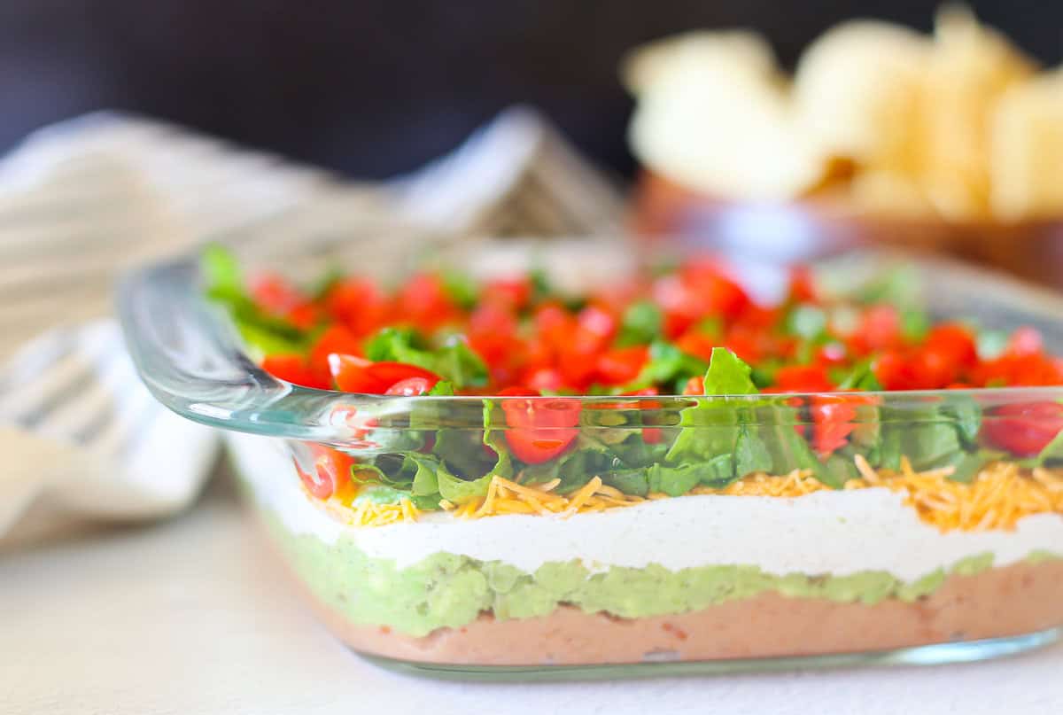 Layered taco dip in a square glass dish.