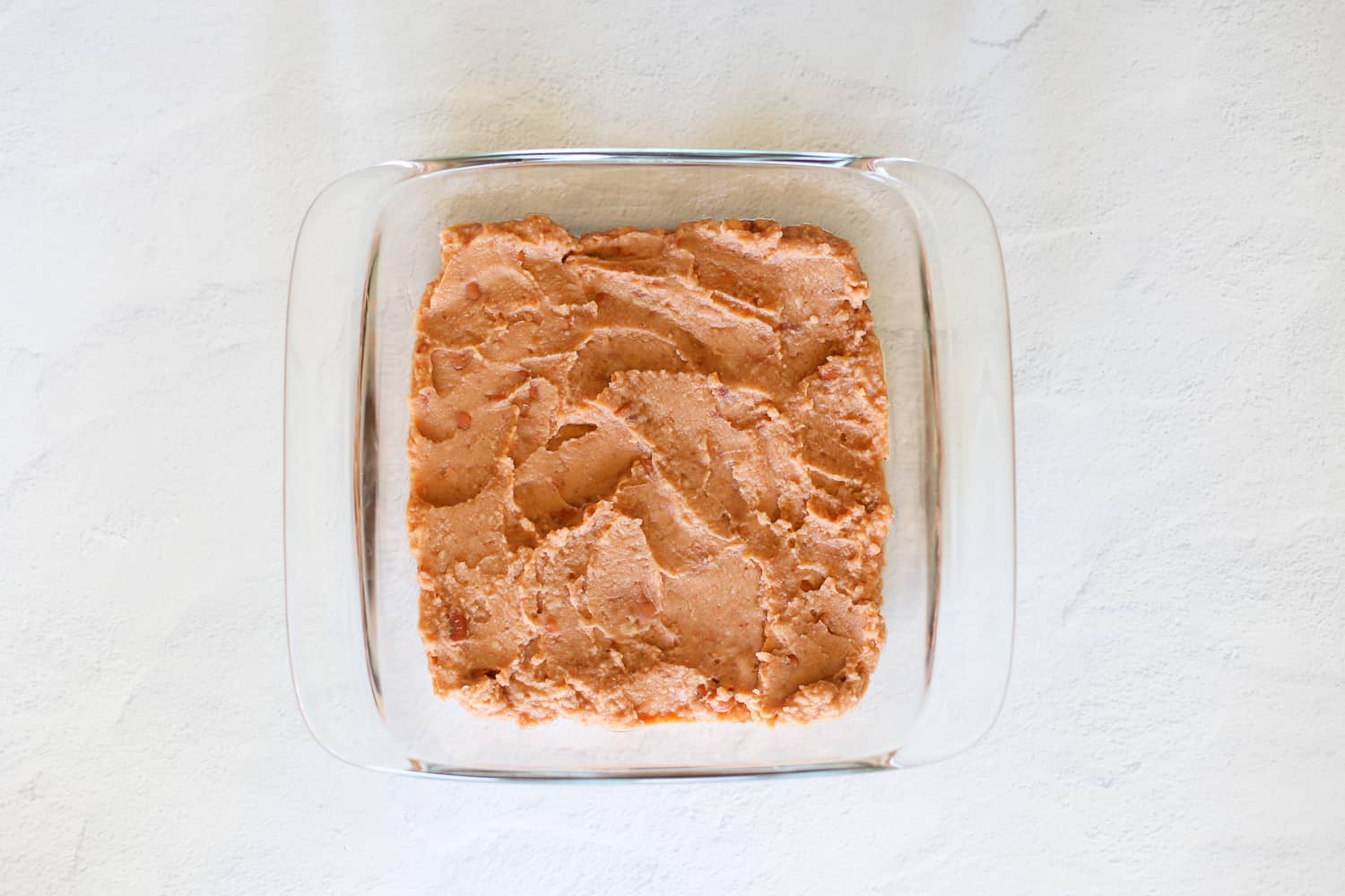 Refried beans spread out in the bottom of an 8x8 baking dish.