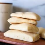 Panini bread stacked up on a wooden cutting board.