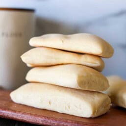 Panini bread stacked up on a wooden cutting board.